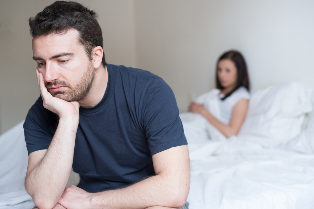 disappointed man sitting on bed away from girlfriend.